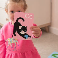 Load image into Gallery viewer, Child holding a pink card with a black cat illustration and 'Cc' letter