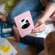 Load image into Gallery viewer, Person holding a card with a cow illustration while sitting on the floor with educational cards.