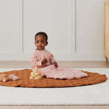 Load image into Gallery viewer, Child sitting on a brown mat wearing Daisie patterned Ergo Pouch with toys in a room.