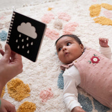Load image into Gallery viewer, Baby lying on a colorful rug with a person holding a book with a cloud and raindrop design.
