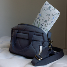 Load image into Gallery viewer, Blue quilted handbag with floral-patterned changing mat on a white surface
