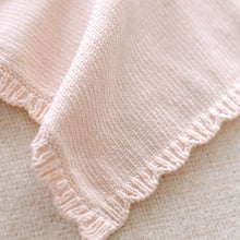 Load image into Gallery viewer, Close-up of a pink knitted blanket on a textured surface