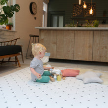 Load image into Gallery viewer, Child playing with toys on a patterned rug in a room with wooden cabinets and a clock.