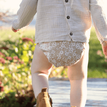 Load image into Gallery viewer, Toddler wearing a light-coloured shirt and floral-patterned cloth nappy outdoors with flowers in the background