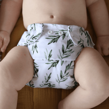 Load image into Gallery viewer, Baby wearing a white cloth nappy with green leaf pattern on a wooden floor