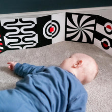Load image into Gallery viewer, Baby lying on a carpeted floor in front of a wall with black and white patterned panels.
