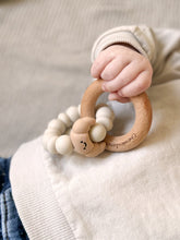 Load image into Gallery viewer, Child's hand holding a wooden teething ring with beads
