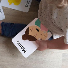 Load image into Gallery viewer, Child holding a card with a cartoon face labeled 'Mama' on a wooden surface.
