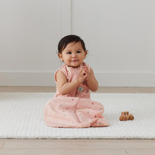 Load image into Gallery viewer, Baby in a pink Daisie design ErgoPouch sitting on a white mat with a wooden toy car.
