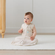 Load image into Gallery viewer, Baby in a beige sleeveless outfit sitting on a white mattress.
