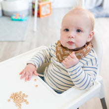 Load image into Gallery viewer, Baby sitting in a high chair with scattered food, wearing mudcloth patterned bandana bib and a striped shirt.
