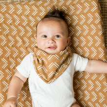 Load image into Gallery viewer, Baby wearing a white onesie and mudcloth pattern bandana bib on a patterned blanket
