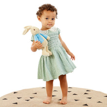 Load image into Gallery viewer, Child in a light green dress holding a plush toy on a round beige rug with black triangle patterns.
