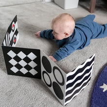 Load image into Gallery viewer, Baby playing with a black and white patterned sensory board  on a carpeted floor.
