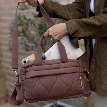 Load image into Gallery viewer, Person holding a brown quilted changing bag with a phone case on a blurred background
