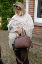 Load image into Gallery viewer, Woman holding a baby wrapped in a blanket with a brown bag, standing outdoors.
