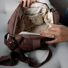 Load image into Gallery viewer, Person opening a brown changing bag  on a light grey surface
