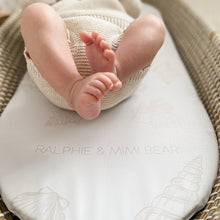 Load image into Gallery viewer, Baby legs on seashell basket liner with 'Ralphie &amp; Mimi Bear' branding, on a woven surface.
