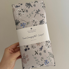 Load image into Gallery viewer, Floral-patterned travel changing mat held by a hand with a neutral background
