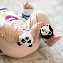 Load image into Gallery viewer, Baby wearing panda-themed ankle rattles on a light-coloured floor
