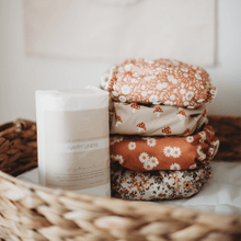 Load image into Gallery viewer, Stack of floral-patterned cloth nappies on a white surface with a wicker basket in the background.
