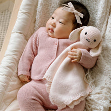 Load image into Gallery viewer, Baby in pink outfit holding a plush toy on a soft surface
