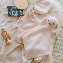 Load image into Gallery viewer, Baby outfit with blush pink bunny comforter, hat, and wooden rattle on a textured surface.
