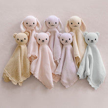 Load image into Gallery viewer, Seven knitted cuddle+kind blankets in soft pastel colours, including beige, cream, pale pink, blush, and light blue, arranged on a neutral beige background.
