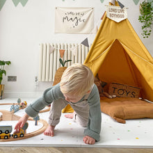 Load image into Gallery viewer, Child playing with a toy train set in a room with a yellow teepee and decorative banners.
