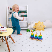 Load image into Gallery viewer, Child playing with colorful stacking toys in a room with a bookshelf and sun-shaped pillow.
