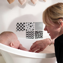 Load image into Gallery viewer, Woman interacting with a baby in a white bathtub with black and white patterned tiles on the wall.
