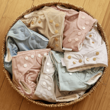 Load image into Gallery viewer, Basket of baby cloth nappies with buttons in various colours on a wooden floor
