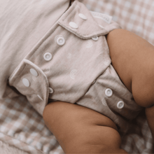 Load image into Gallery viewer, Close-up of a baby wearing a patterned beige cloth nappy with button details on a soft, blurred background.

