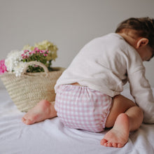 Load image into Gallery viewer, Child wearing a pink checkered cloth nappy sitting on a bed with flowers in the background
