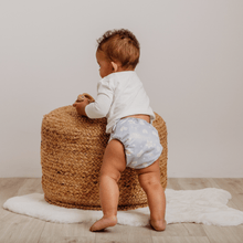 Load image into Gallery viewer, Baby in a cloth nappy standing next to a woven stool with a neutral background
